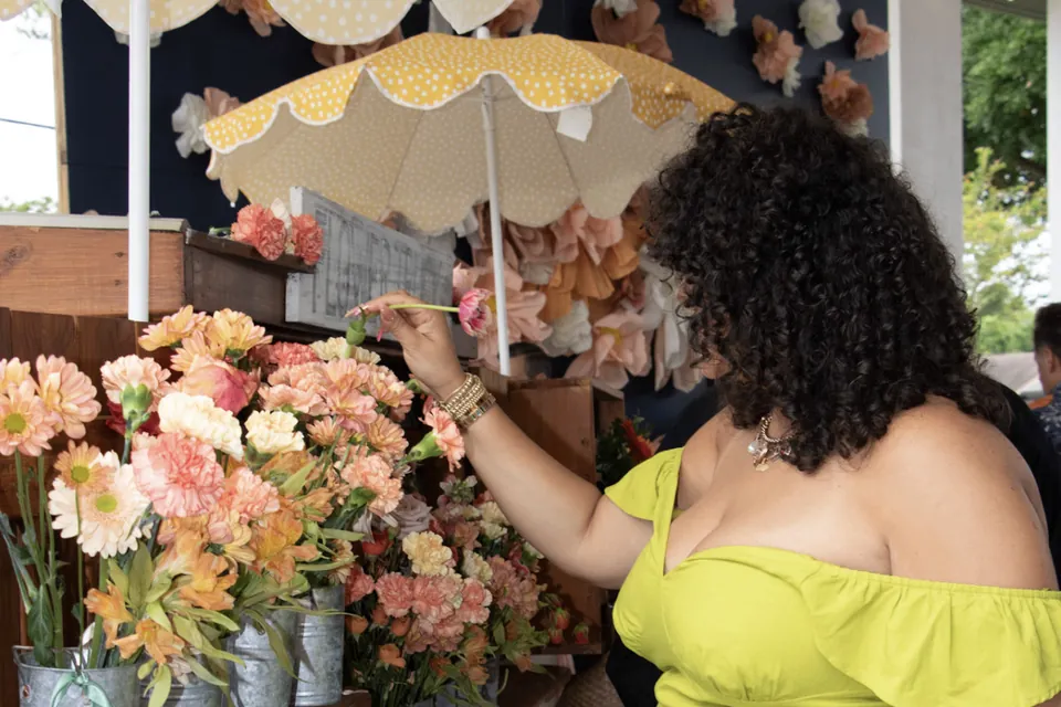 A guest choosing a fresh stem from buckets of peach and coral blooms on the flower truck