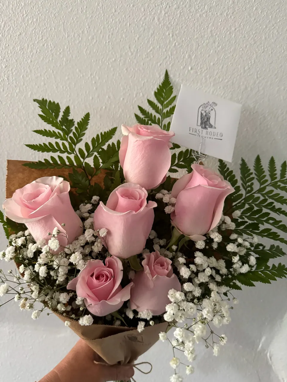 A hand holding a bouquet of pink roses with baby’s breath and fern