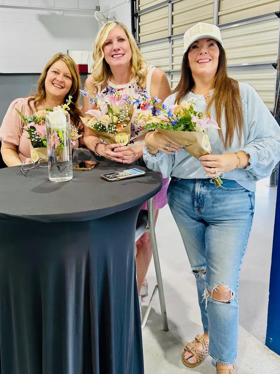 Three smiling guests holding the bouquets they built at an indoor event